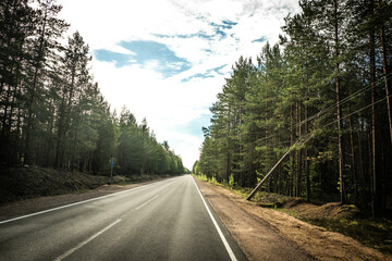 Fototapeta premium The road among the Karelian taiga. Pine forest on the side of the road. Trip to Karelia. Highway among the trees. Driving on a trip to beautiful places. Karelia. Day.