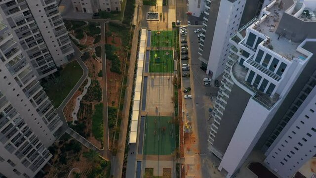 Aerial Tilt Up Shot Of Sports Courts Amidst Buildings Structures, Drone Flying Forward Over Beach Against Sky - Netanya, Israel