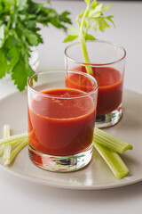 Two glasses with tomato juice, parsley and selera on a white background
