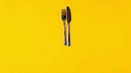 Time to eat, fork knife, alarm clock on yellow background. Stop motion animation, top view