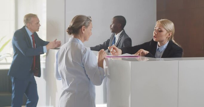 Mature businesswoman signing document at reception desk in business center
