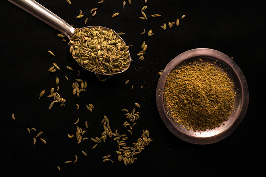 Top view spoon of cumin and a bowl of ground cumin on a black surface