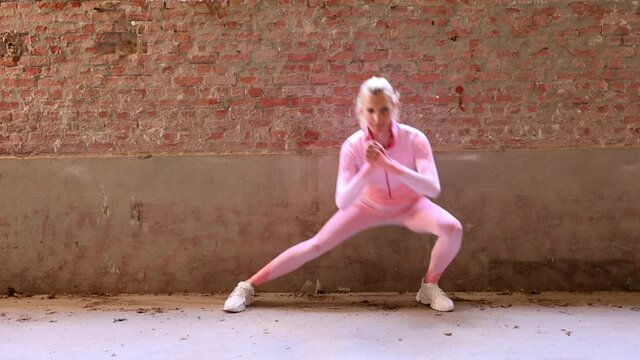 Beautiful fit young female athlete wearing pink sports clothing performs side lunges work out her legs in the gym. Beautiful woman doing sports. High quality FullHD footage