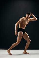 Obraz premium sexy man with a pumped up naked body in black panties posing against a dark background