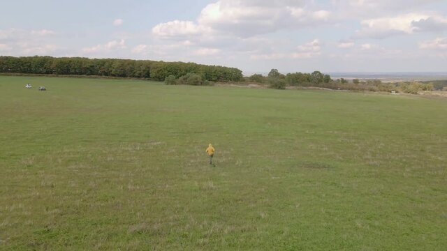 View from above. A guy in a yellow sweater runs across a green field. A young man in sportswear runs cheerfully across the summer field.