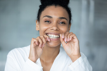 Happy excited millennial Black girl using thin mint thread, floss for cleaning teeth, smiling at camera, showing white healthy teeth, keeping routine for dental care, fresh breath. Close up portrait