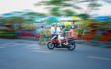 Ho Chi Minh City, Vietnam - February 9, 2021: People Vietnamese driving a motorbike with holder flower or kumquat pot behind decoration purposes house for Lunar new year in Ho Chi Minh, Vietnam