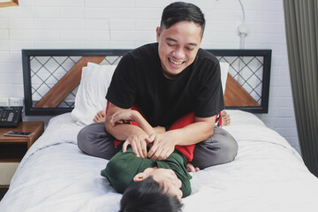Cheerful boy laying on the bed having fun and playing together with his father