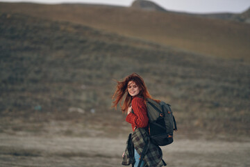 woman in a red sweater and jeans with a backpack on her back are resting in the mountains in nature