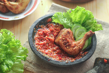 Ayam penyet (smashed fried chicken) is Indonesian East Javanese cuisine, served with sambal chili, lettuce and cucumber slice.