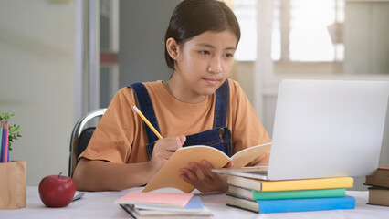 Student studying and writing notes in a notebook at home, making research on laptop and browse internet, watching online webinar, listening audio course, e-learning education concept