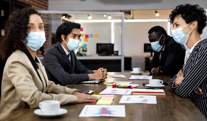 Multiracial mixed race businesspeople group working with concentration  at office, wearing face masks as new normal to protect or prevent virus in pandemic crisis, using laptop and job discussion.