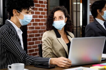 Multiracial mixed race businesspeople group working with concentration  at office, wearing face masks as new normal to protect or prevent virus in pandemic crisis, using laptop and job discussion.