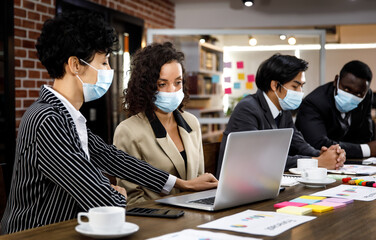 Multiracial mixed race businesspeople group working with concentration  at office, wearing face masks as new normal to protect or prevent virus in pandemic crisis, using laptop and job discussion.