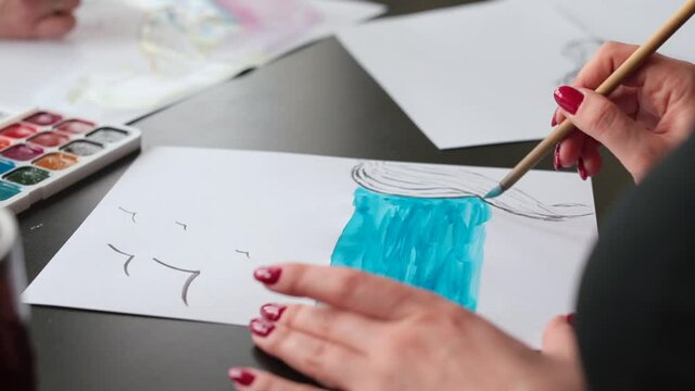 The hand of a talented artist makes a drawing with blue paint. She smears on the dye. The technique of performing the image using watercolour.