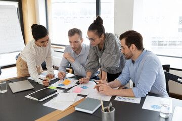 Diverse employees team coworkers discussing project strategy, working with documents, analyzing...