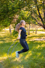 Young woman jumping rope on the lawn in a summer park. Jumping model. The concept of a healthy lifestyle and outdoor sports.