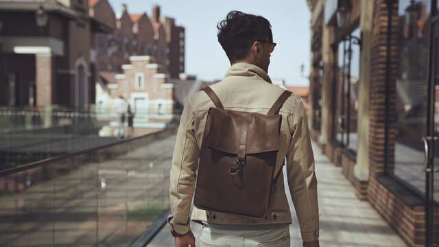 back view of stylish man with leather backpack walking outside.