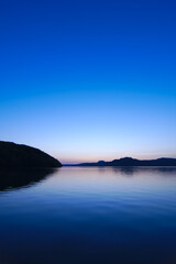 Fototapeta na wymiar 薄い青に染まるトワイライトの湖と空。