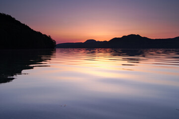 薄いオレンジ色の夜明けに穏やかな湖面の湖。