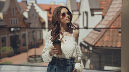 stylish young woman in sunglasses holding coffee to go outside.