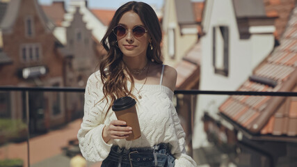 stylish young woman in sunglasses holding coffee to go outside.