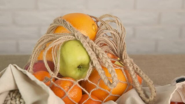 Eco products in a bag. A view of fresh apples and oranges in eco string bag on the table in the kitchen.