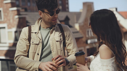 stylish couple in sunglasses holding paper cups and talking outside.