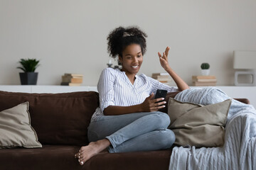 Smiling young african american multiracial woman holding cellphone in hands, recording streaming video in social networks application or enjoying pleasant distant mobile webcam zoom conversation.