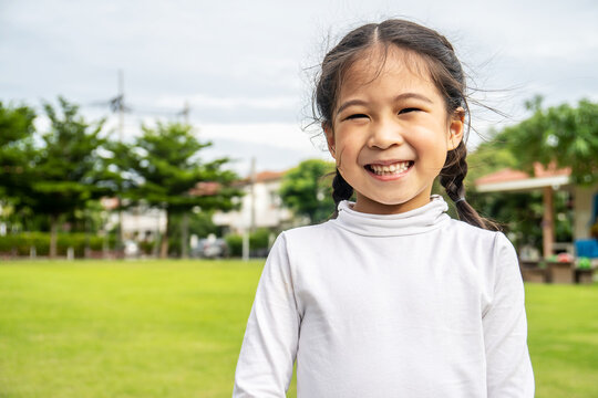 Portrait of Cute asian little girl standing in summer park looking in camera smiling happily, Laughing child, Expressive facial expressions.
