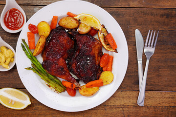 Homemade Baked Chicken Drumstick with Potatoes in a white plate on an old wooden table.