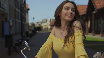pleased young woman with wavy hair smiling near motorcycle.