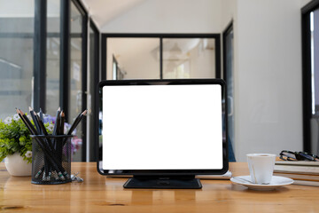 Fototapeta premium Front view computer tablet with white screen, pencil holder and coffee cup on wooden table.