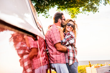 Fototapeta premium Travel people have fun hugging together outdoor with red old van vehicle - adult man kissing cheerful happy middle age woman - table with food and clear sky in background