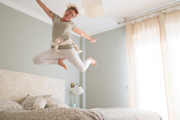 Young adult pretty woman go crazy for happiness and jump on the bed with coffee cup - overjoyed...