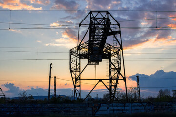 High voltage lines and a huge metal construction, and concrete fence with graffiti at colorful sunset sky background