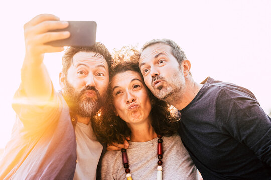 Group of three adult young friends take selfie picture doing nice expression - middle age people use cellphone to take a picture - concept of friendship and cheerful happy friends