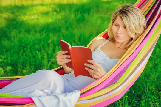happy girl reading a book in a hammock outdoors in the park