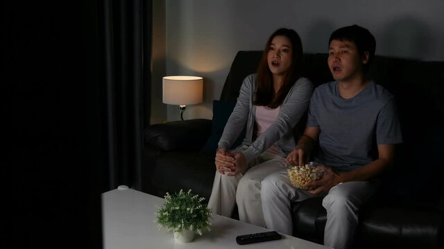 Crying young couple watching romantic movie TV on sofa at night