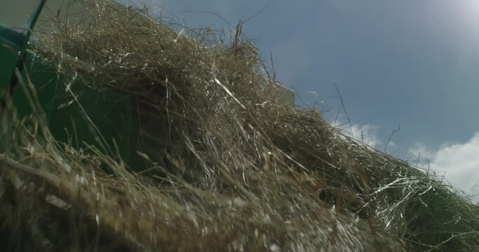 Slow motion low angle of a Hustler Chainless breaking apart a hay bale and unrolling it back into a windrow