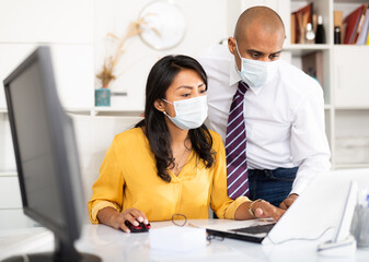 Portrait of businessman with female colleague working in office in medical face masks to prevent spread of viral infection. New life reality