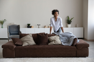 Joyful millennial african american woman posing in modern stylish living room interior, looking at camera. Sincere happy mixed race biracial lady feeling excited of moving into new rent apartment.