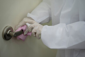 Worker in protective suit wiping door handle with disinfectant