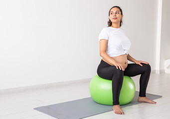 A young pregnant woman doing relaxation exercise using a fitness ball while sitting on a mat....