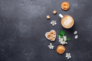 Cup of coffee with cakes and spring flowers on dark stone background. Top view. Copy space for your text
