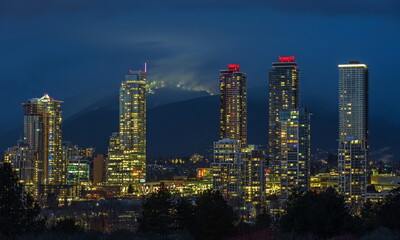 Fototapeta na wymiar View of the new residential high-rise residential area in Burnaby City at night, against the backdrop of illuminated ski slopes on the mountain range
