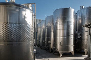 Stainless tanks for processing and fermentation wine production in the open air with blue sky background. Modern wine factory