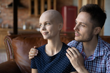 Thoughtful husband giving support and empathy to hairless wife with cancer. Man hugging ill...