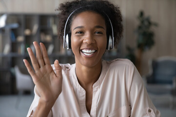 Smiling attractive young african american woman in headphones looking at camera, waving hands,...