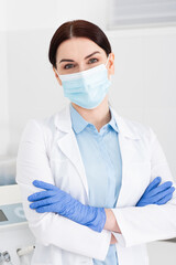 dentist in latex gloves and medical mask standing with crossed arms in dental clinic.